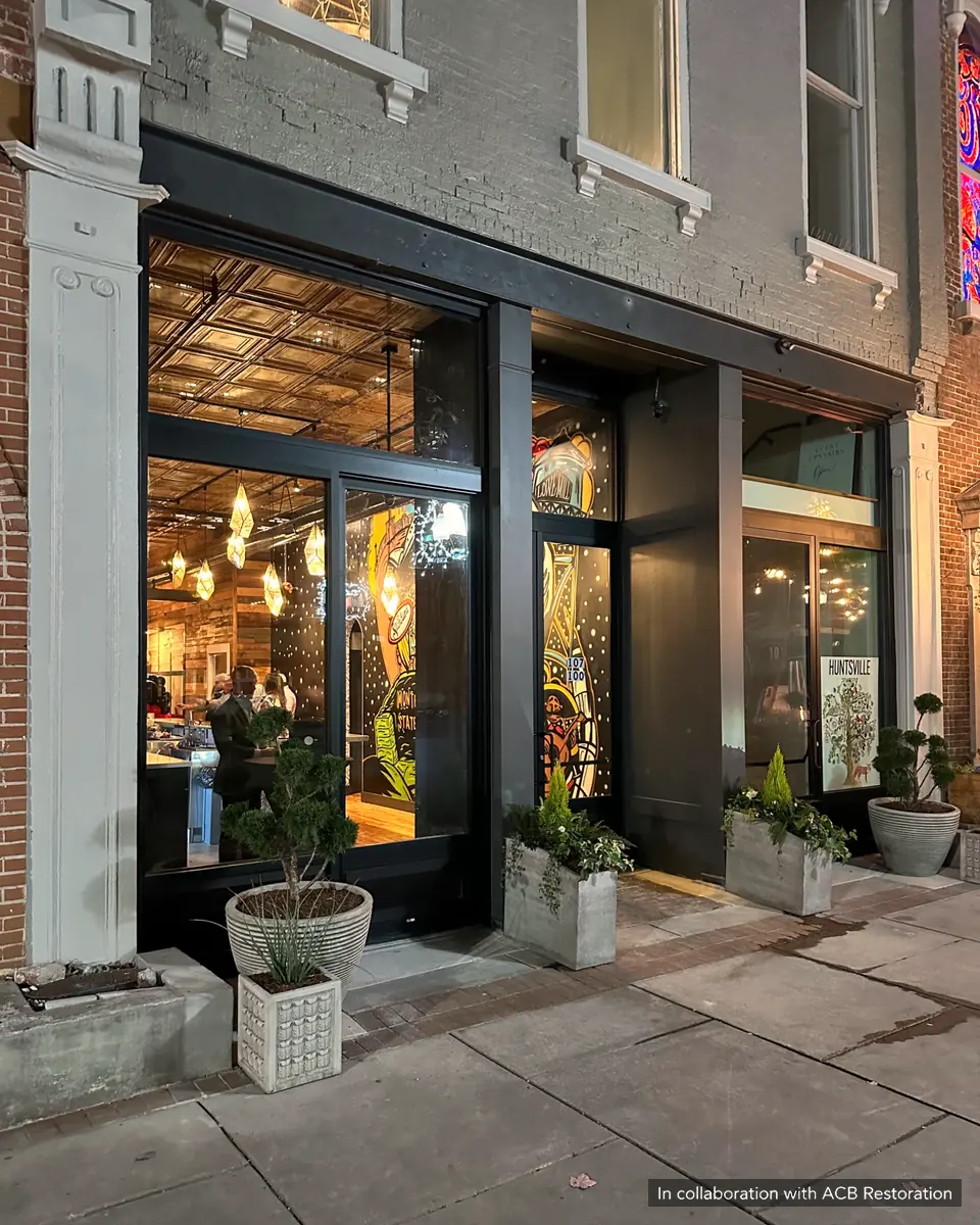 Illuminated restaurant storefront framed by decorative columns, painted brick and dark window frames. In collaboration with ACB Restoration.