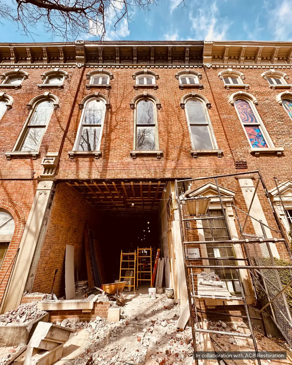 Historic brick facade with arched windows above an open storefront under renovation, with scaffolding and masonry debris. In collaboration with ACB Restoration.