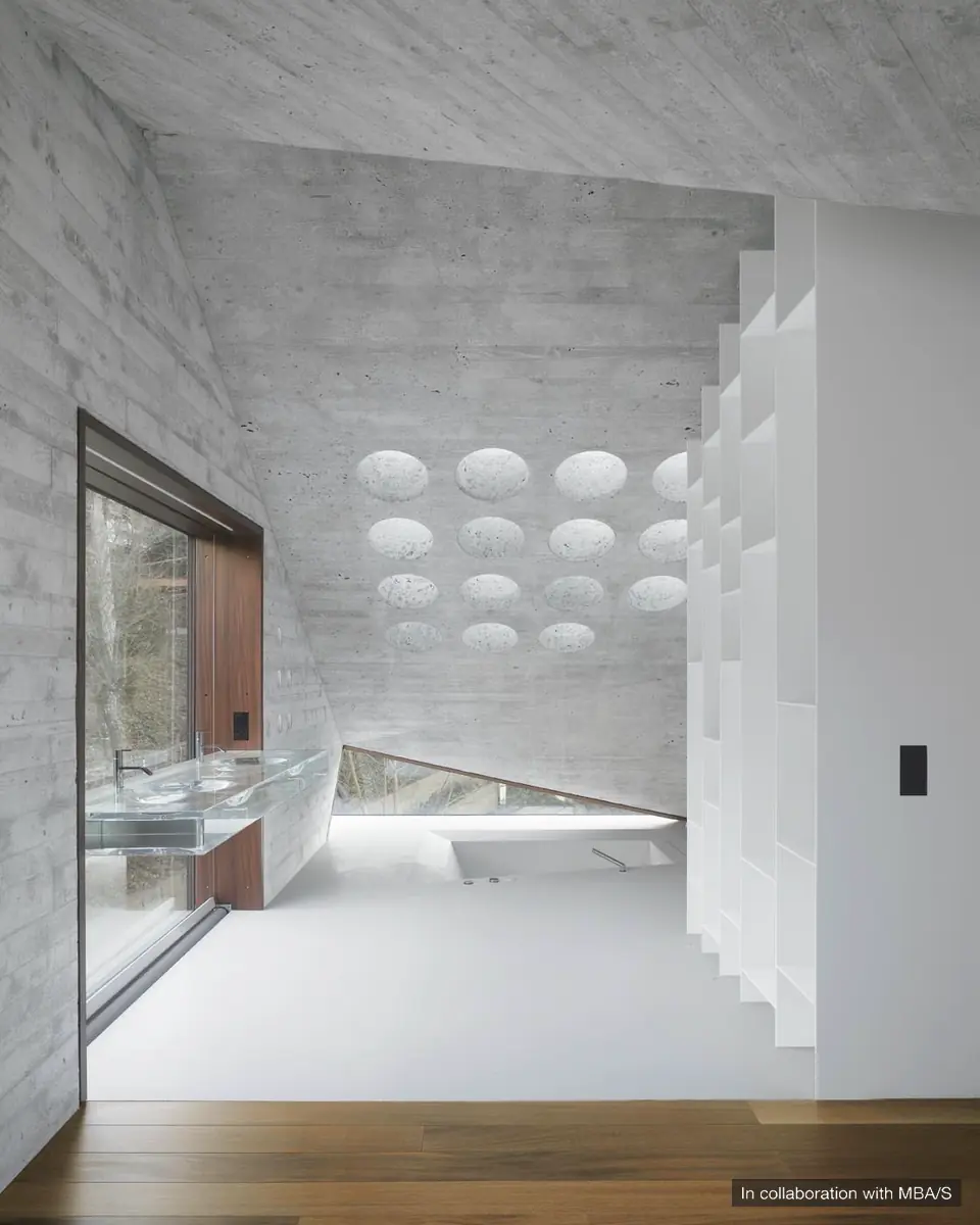 Board-formed concrete bathroom with circular skylights, a glass basin, white shelving and a sunken bathtub. In collaboration with MBA/S.