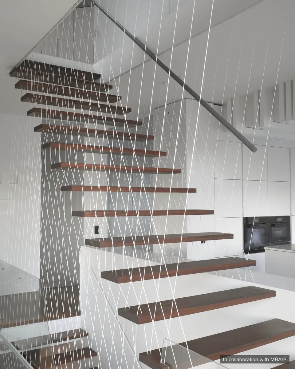 Floating timber stair treads with a fine white cable balustrade, dark handrail and white cabinetry beyond. In collaboration with MBA/S.